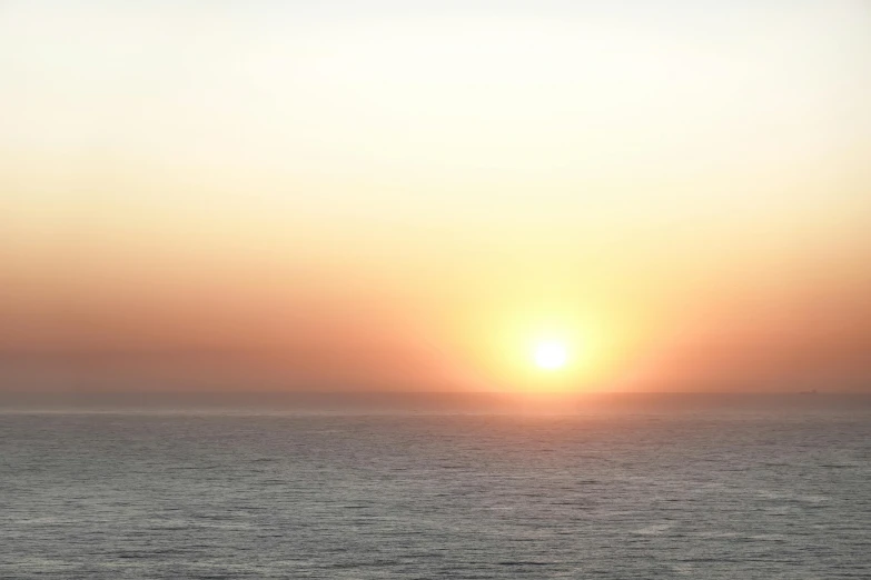 the sun rises over the ocean with surfers in the water