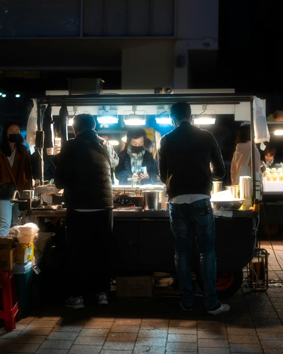 two people standing at a food cart that is lit up