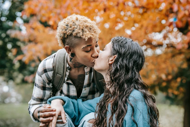 man and woman kissing in front of autumn trees