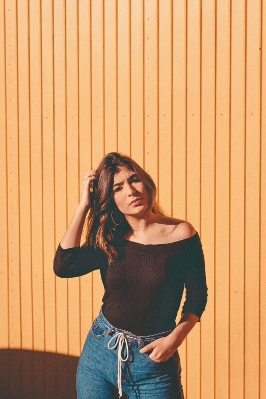 an attractive woman in black top and blue jeans standing in front of yellow wall