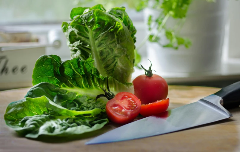 green lettuce and tomatoes sit on a  board next to a large knife