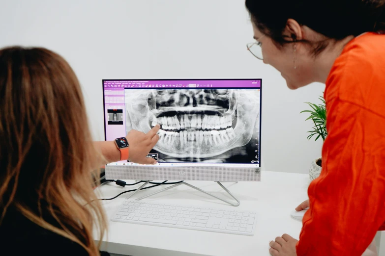a woman shows someone how to see a dental app on a computer