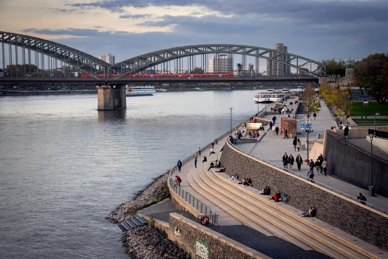 people walking around a river that has a bridge in the background