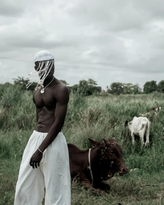 man in white with cow in field near cloudy sky