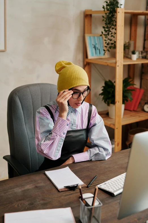 man with yellow hat sitting at table using laptop on cell phone