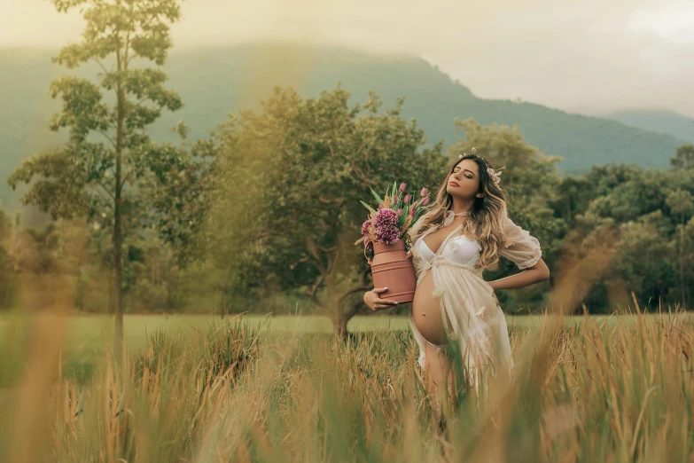 a pregnant woman with flowers on her hands stands in a field