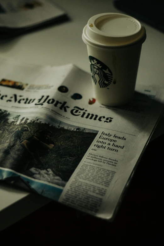 a newspaper sitting on top of a desk next to a cup of coffee