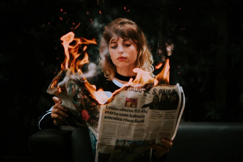 the woman looks down at a piece of newspaper with flames around her