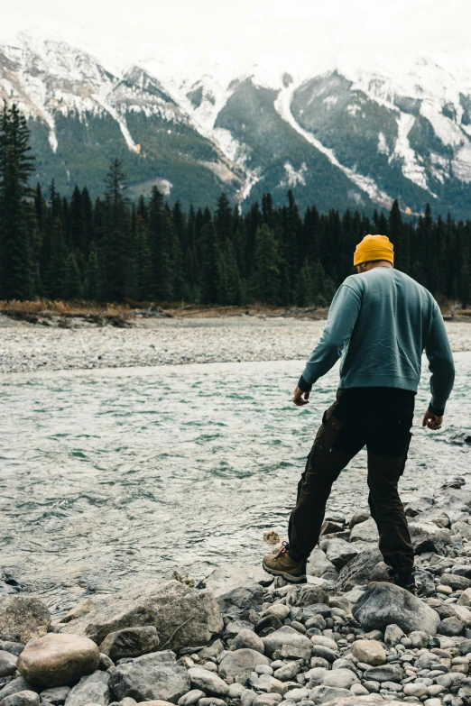 man in fleece walking down the river to cross it