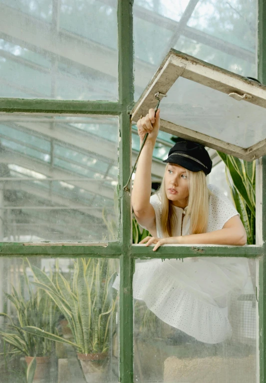 a woman posing with her hat in a greenhouse