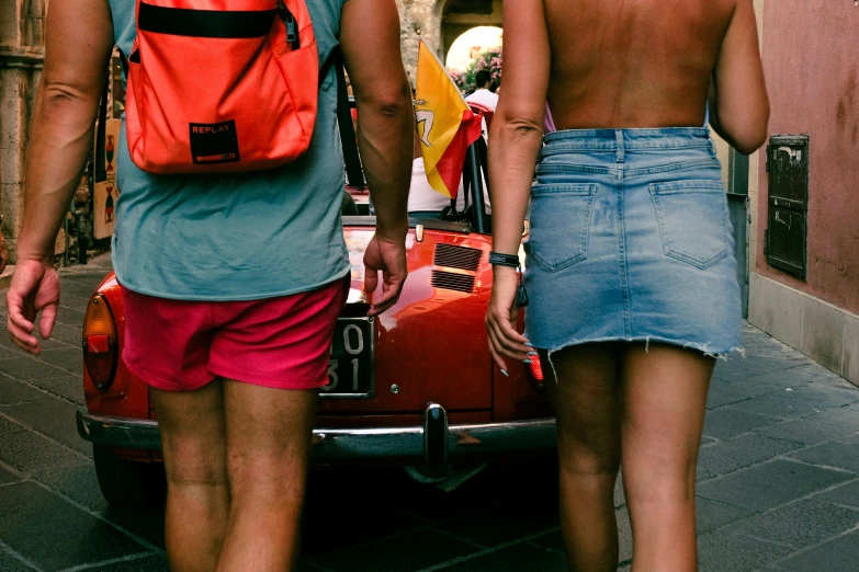 a man and woman with back packs walking towards an old convertible car