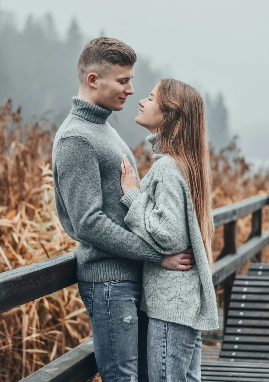 an engaged couple hugging on the boardwalk in a field near trees