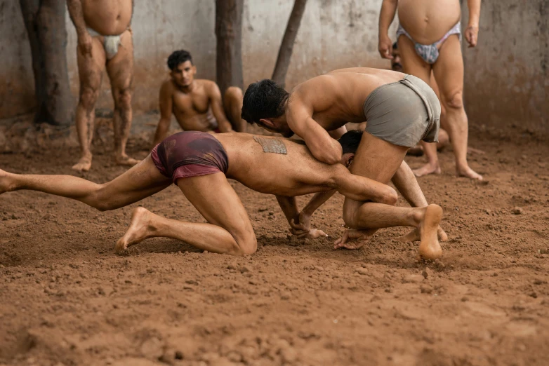 a group of men wrestling on dirt ground