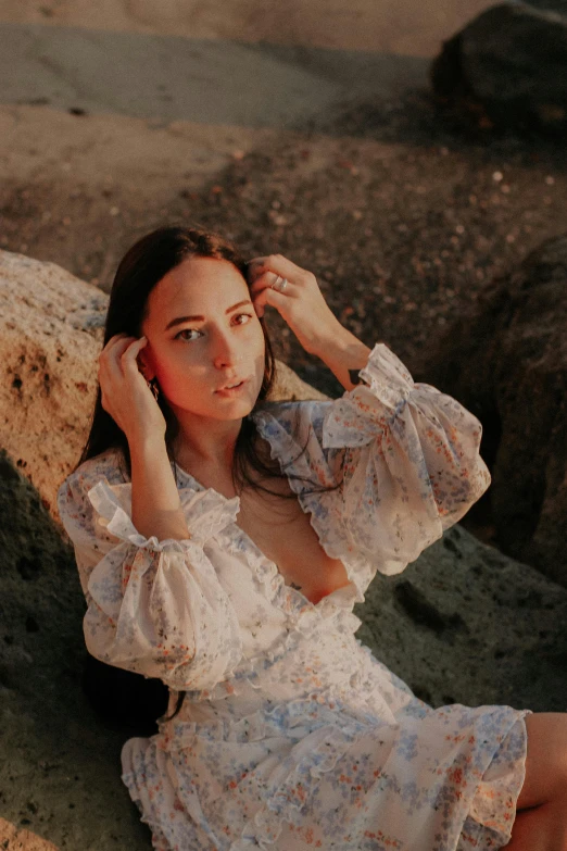 woman in white dress sitting on stone with hand on her head