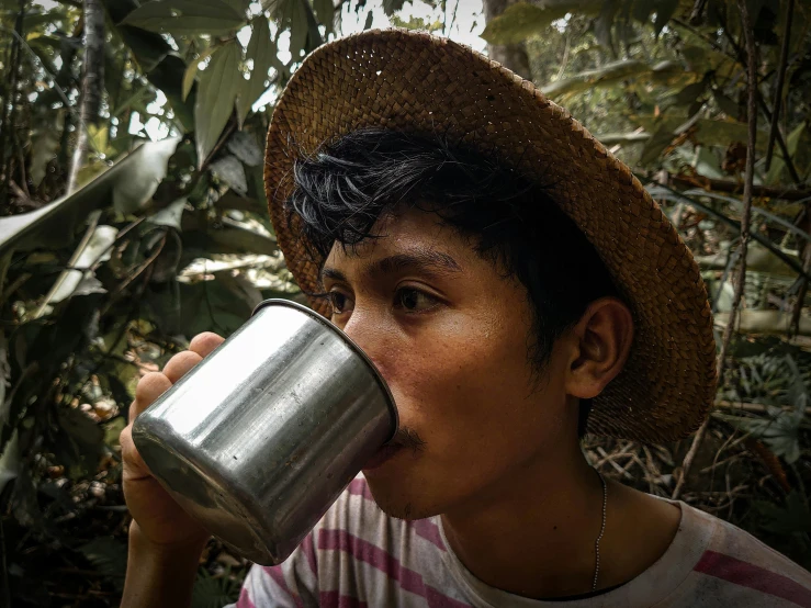 a boy in the woods drinking from a metal cup