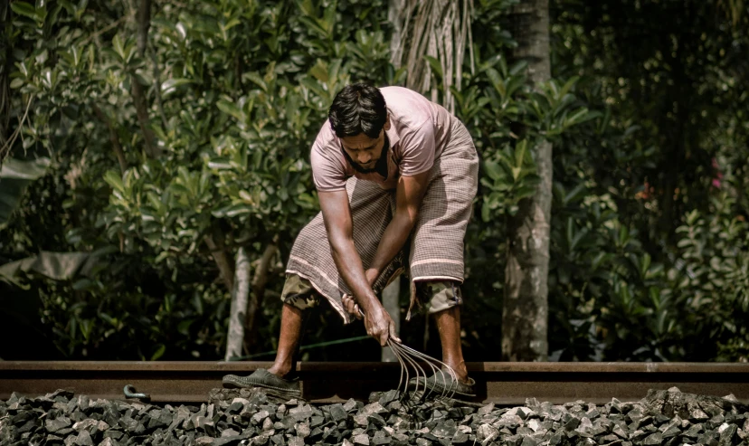 a man shoveling rocks into cement next to trees