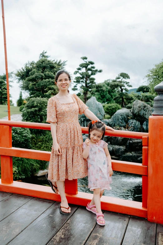 a mother and her little girl standing on a red bridge