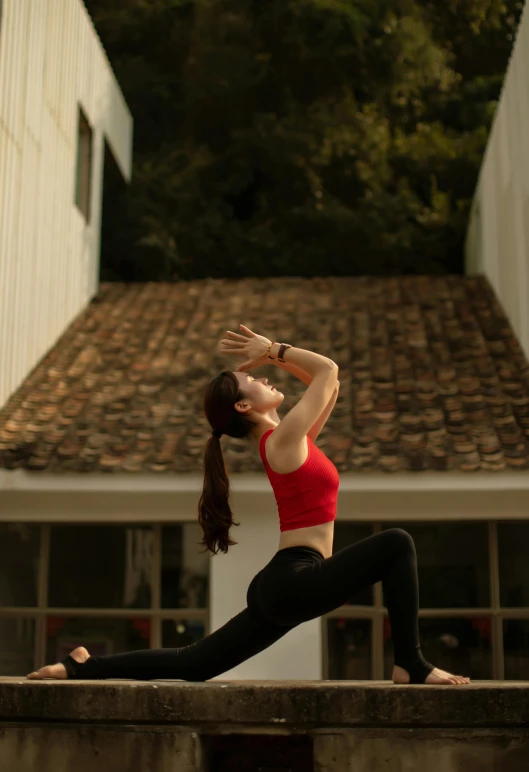 a woman in a red tank top and black leggings is doing yoga outside