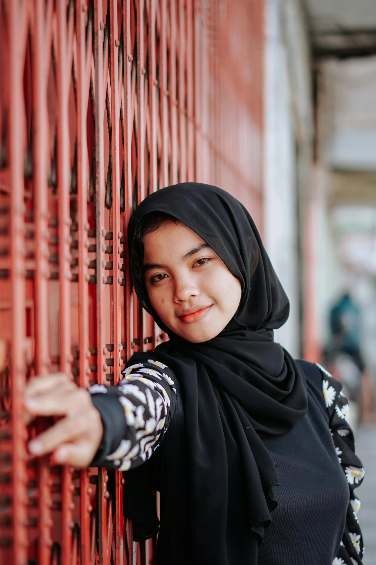 the woman in a headscarf smiles against a red building