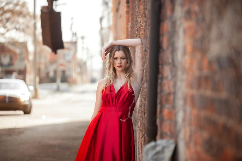 a woman in a red dress leans against a wall