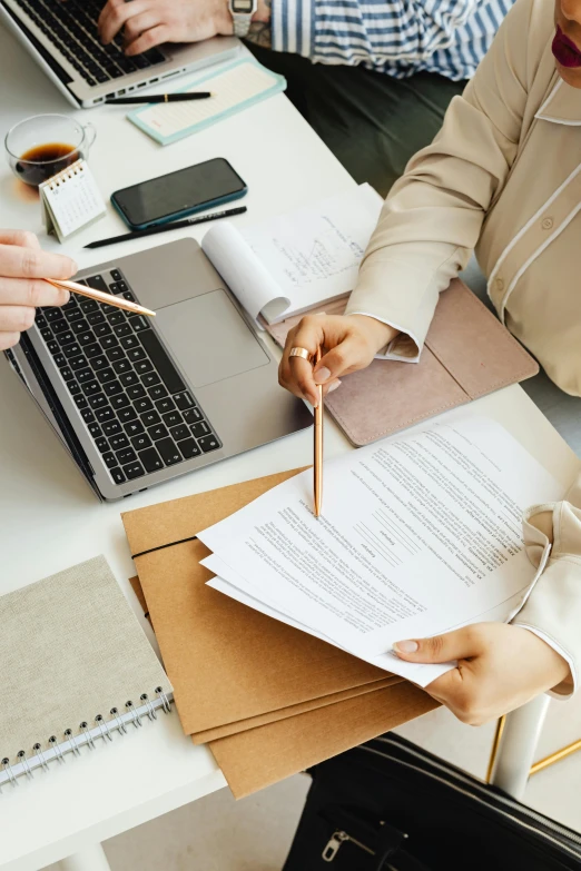 two people sitting at a table with notebooks and papers on their lap tops