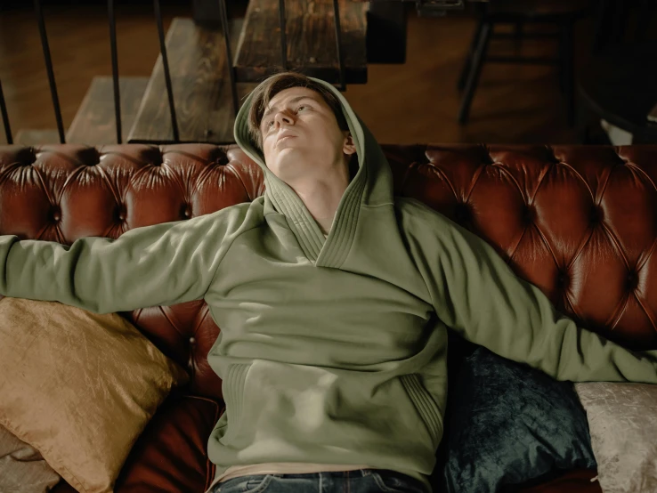 a man wearing a hooded sweatshirt while laying on a sofa