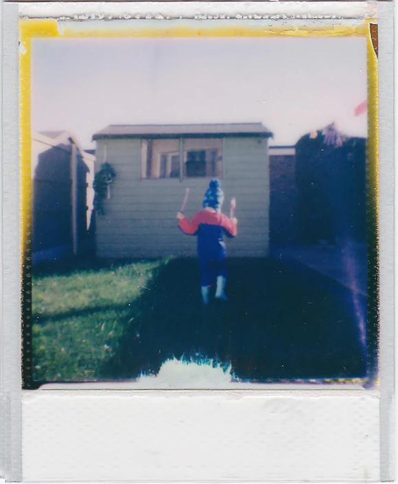 a polaroid frame of a man holding a red object in front of a house