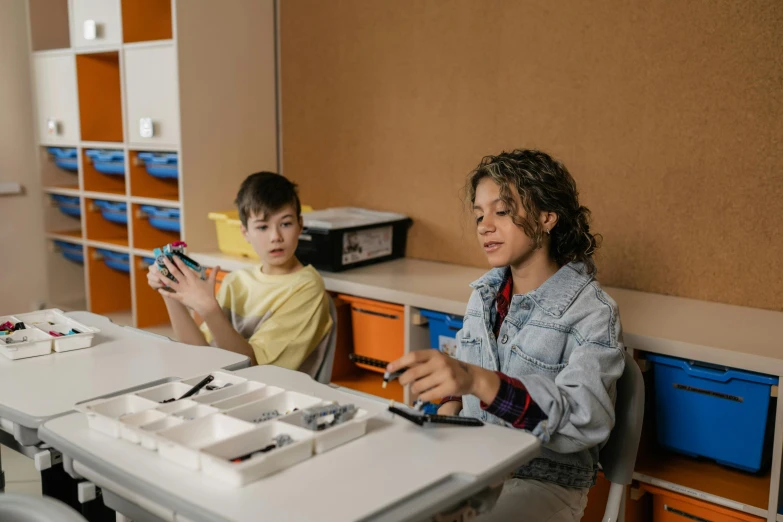 two children sitting at a table and looking at papers