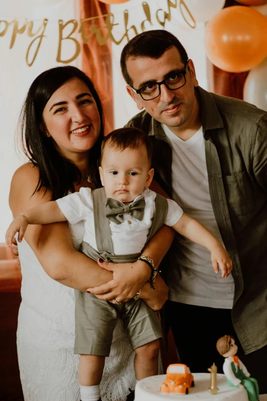 a man and woman stand with a baby next to their cake