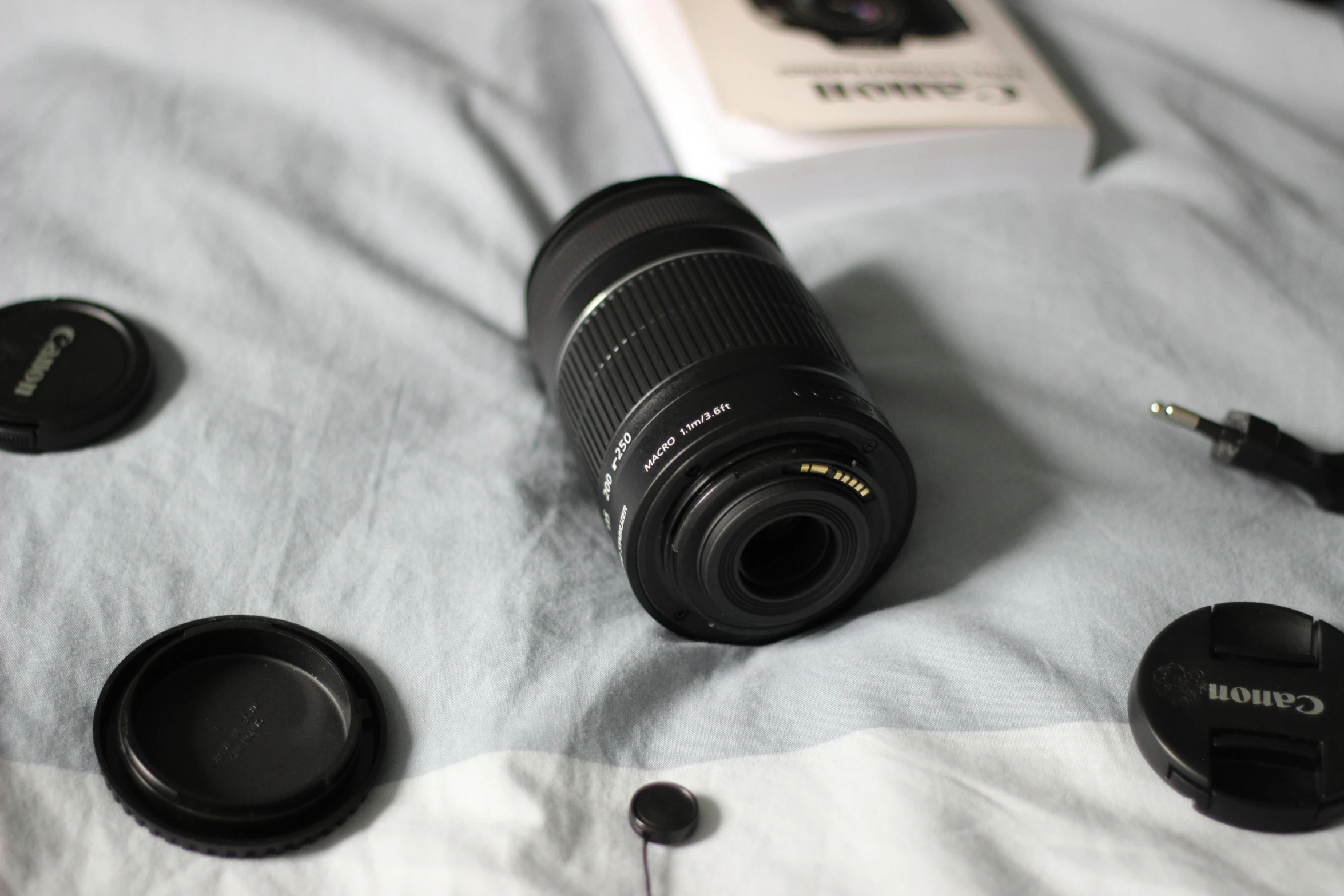 a canon lens is lying on a bed