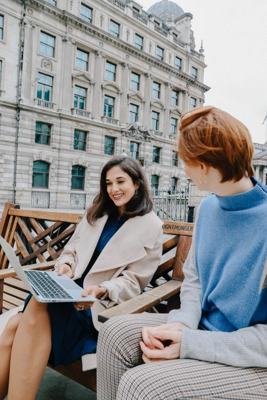 two young women sitting on a bench with an open laptop computer