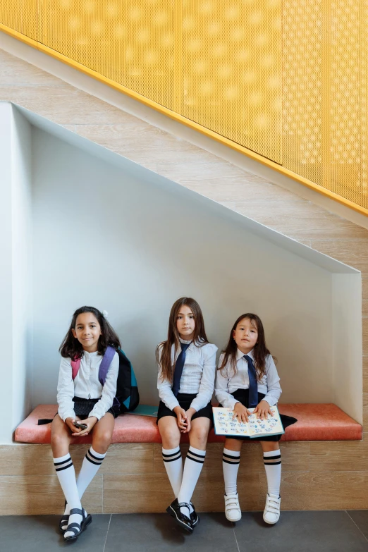 two girls sit on a bench while the girl in the uniform reads a book