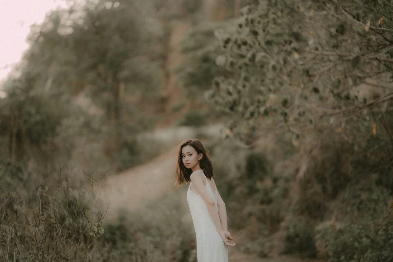 a woman in a dress holding a white bouquet stands on a path surrounded by trees