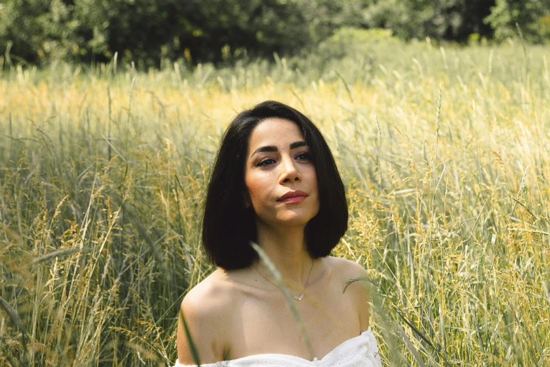 a woman sits in tall grass next to a forest