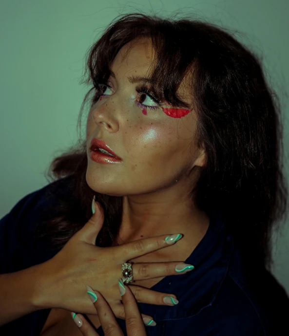 a woman with red and green eyeshadow holding onto her fingers