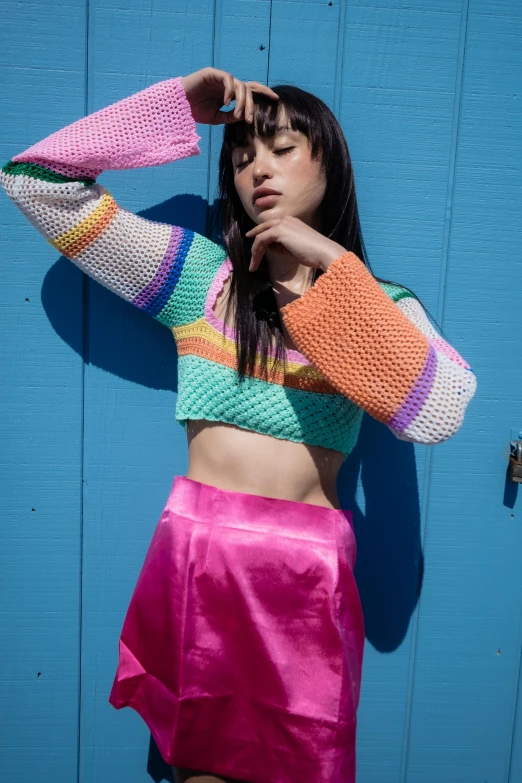 a girl in a colorful top leaning against a blue wall