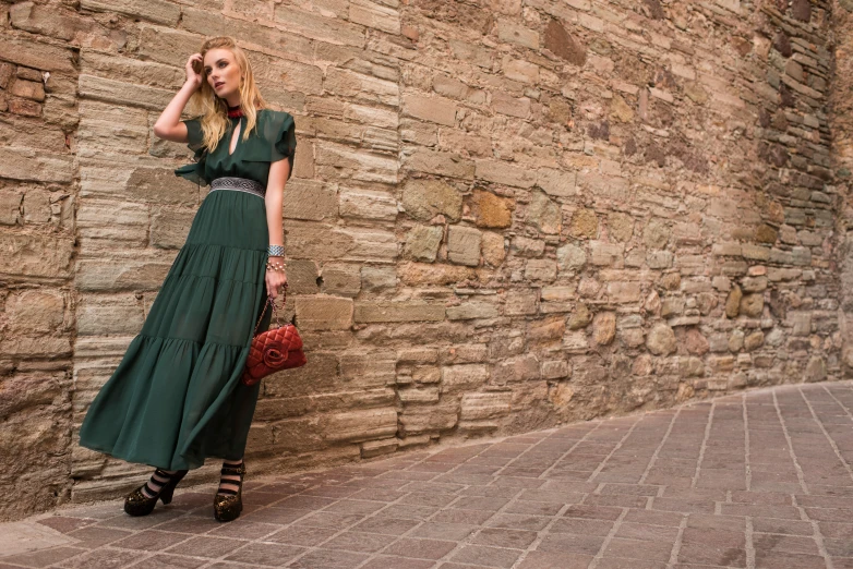 a young woman in green dress leaning against a brick wall