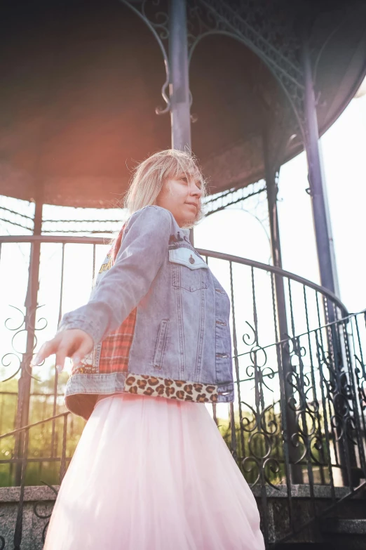 a woman wearing a skirt and jean jacket standing in front of a metal structure