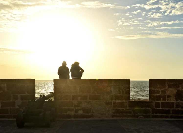 two people standing on a wall with the sun setting in the background