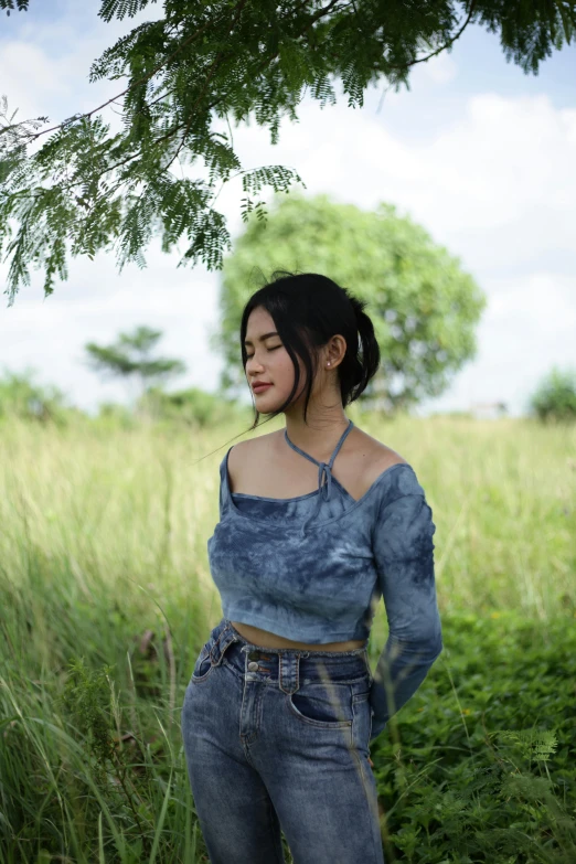 a woman standing in some tall grass under a tree