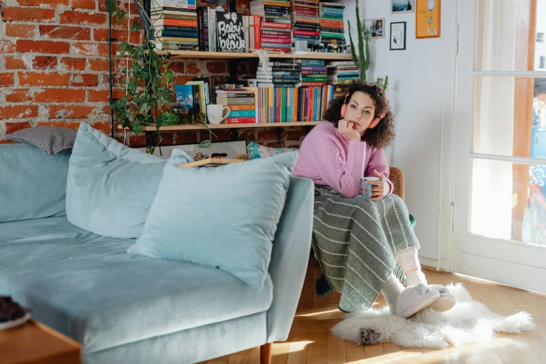 woman sitting in chair with coffee and tea cup next to book shelf