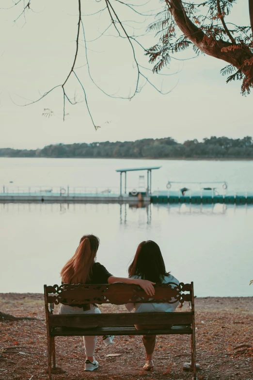two women sit on a bench facing the water
