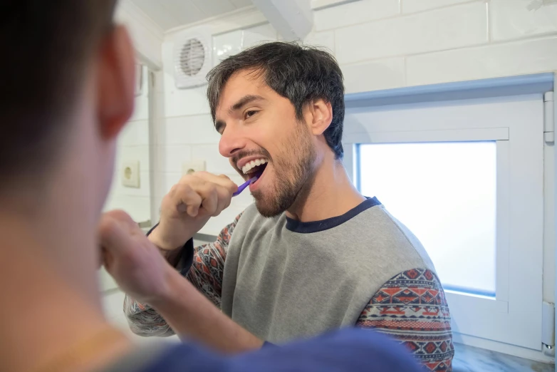 man in grey shirt brushing teeth while another person watches