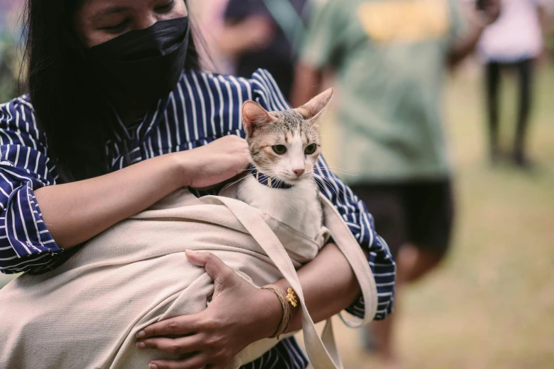 the woman is wearing a black mask while holding a cat