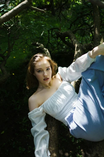 a woman dressed in white leans on a tree trunk and poses