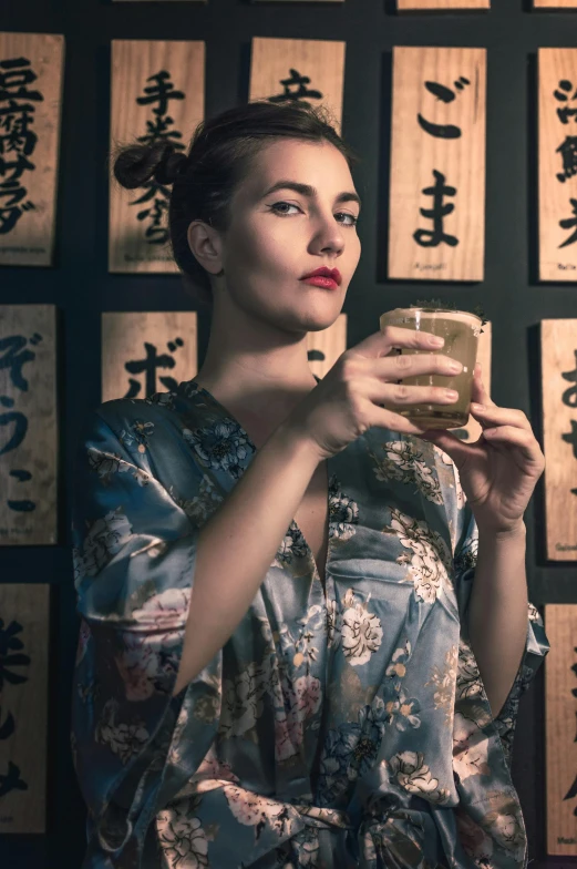 a woman standing in front of a wall holding a cup