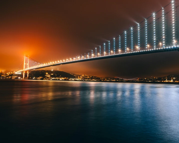 a long suspension bridge spanning over the ocean with night lights on top