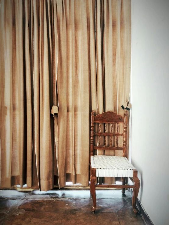 an old chair is in front of a curtained window