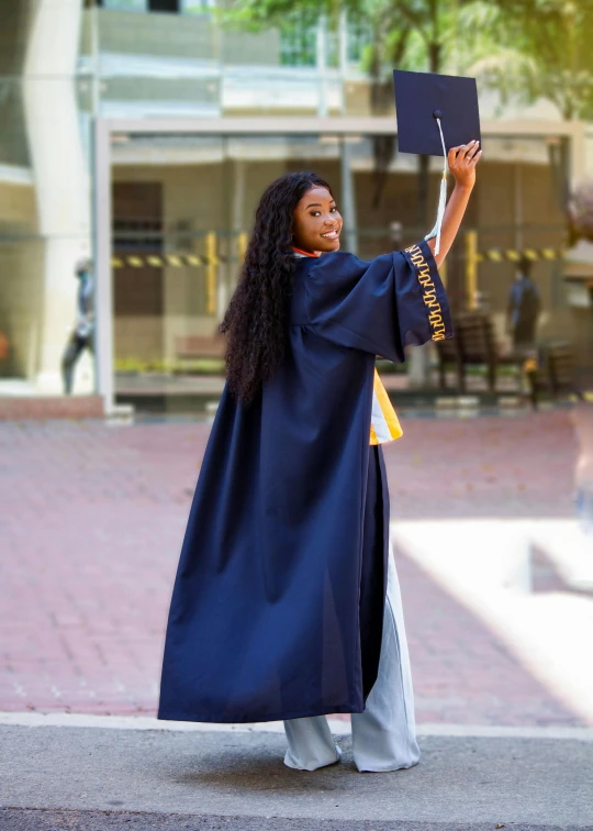 a female student holding up a cap and gown while walking