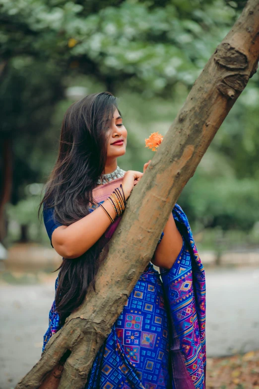 a young woman standing next to a tree holding a leaf